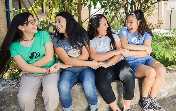 Four girls sitting on a concrete wall. They are creating a Girl Scout friendship cricle with their arms crossed and holding hands.