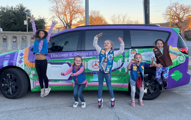 Girl Scouts jumping with the decorative van behind them.