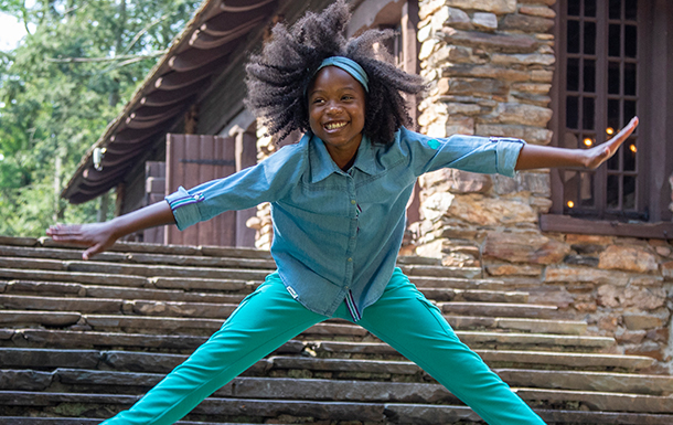 Girl Scout jumping in front of old brick building on a camp property.