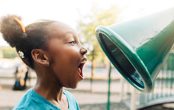 Younger Girl Scout yelling into a talk horn on a playground