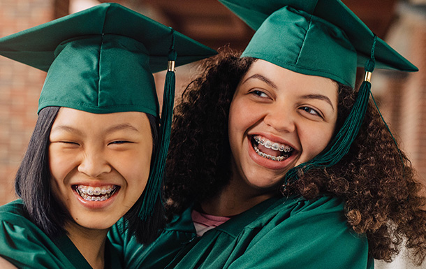 Two girls in emerald green graduation cap and gowns celebrating