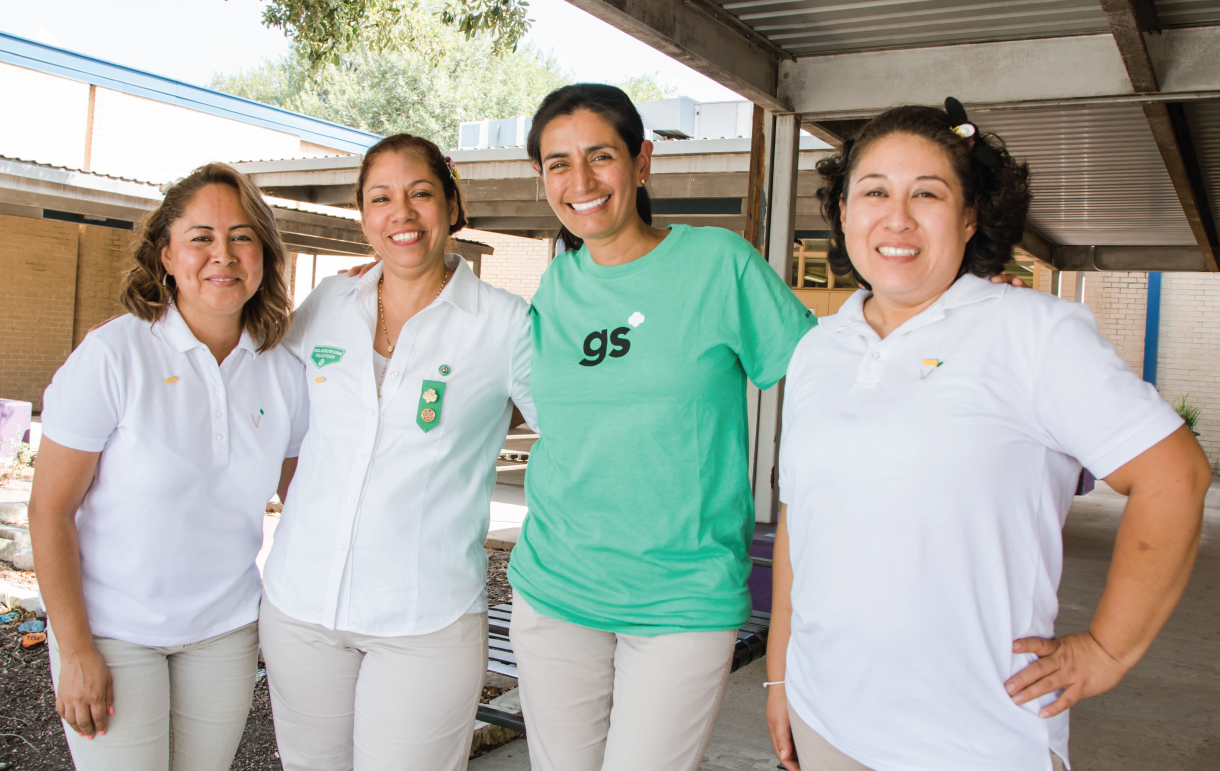 Four adult volunteers smiling linking arms and smiling