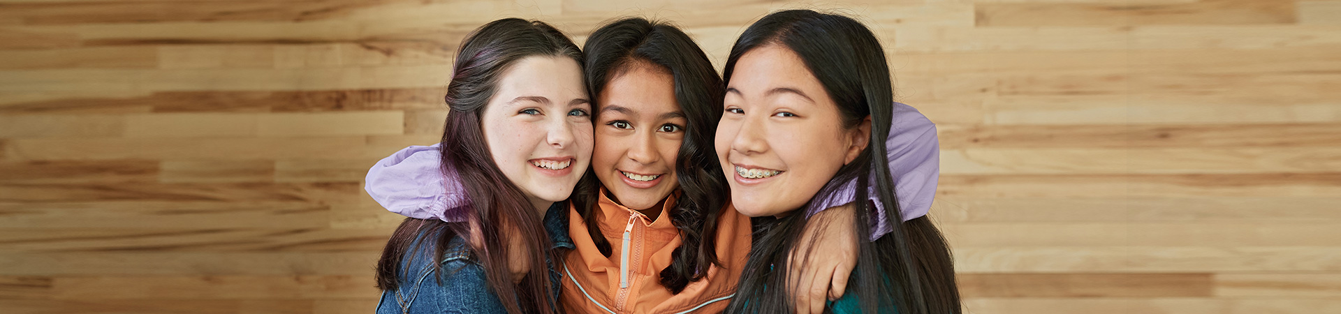  Portrait of three teenage girls. The middle girl has her arms around the necks of the other two in a hug. All three are smiling. 