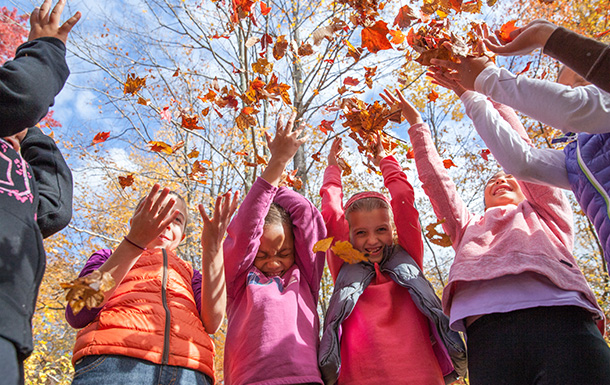 Group of girls throwing autumn leaves into the air on a sunny day.