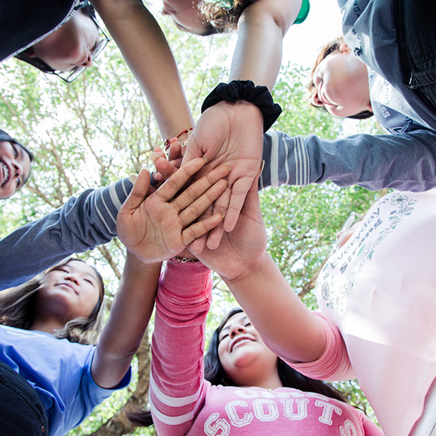 Group of girls in a circle with their hands stacked in the middle.